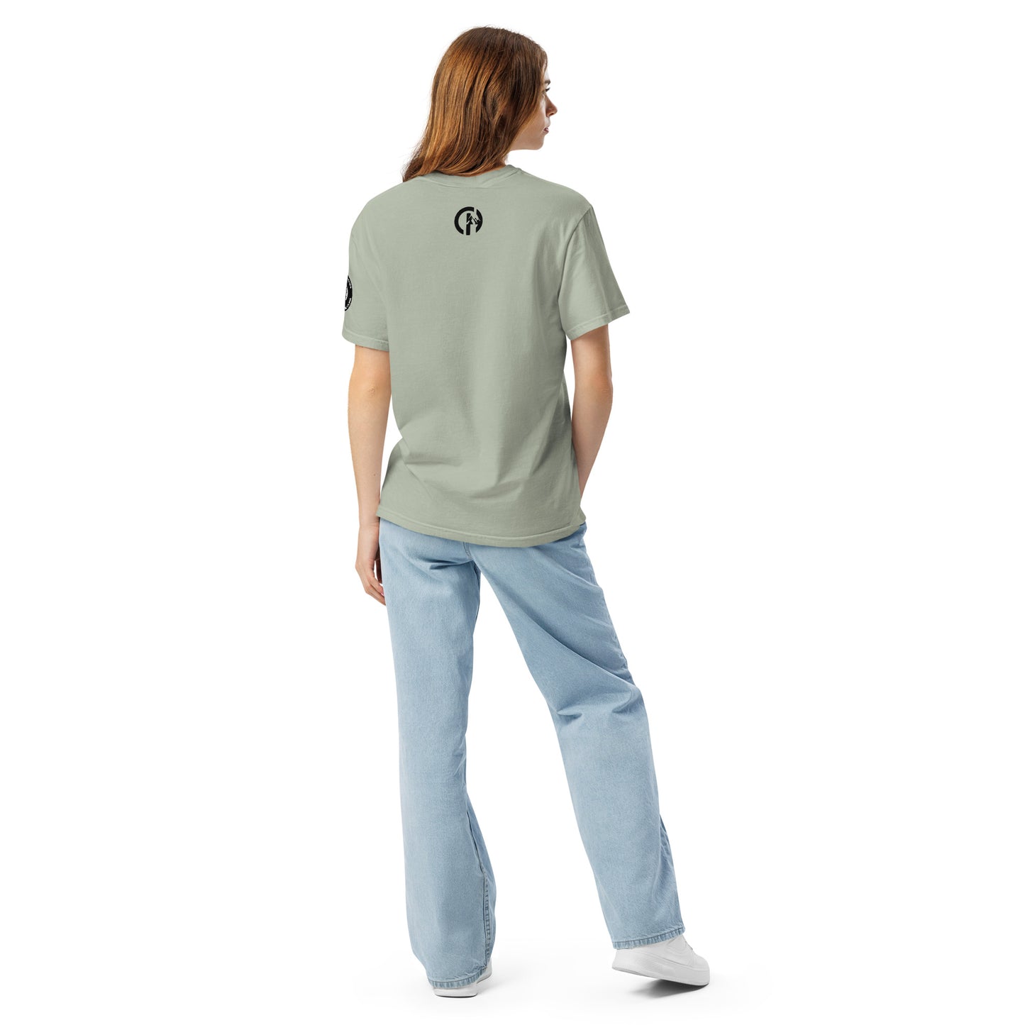 Chillhawk unisex heavyweight short sleeve t-shirt in bay - back view of a lady with light skin and long brown hair, is wearing the t-shirt, light blue jeans, and white sneakers. A circular logo is visible on the back side.