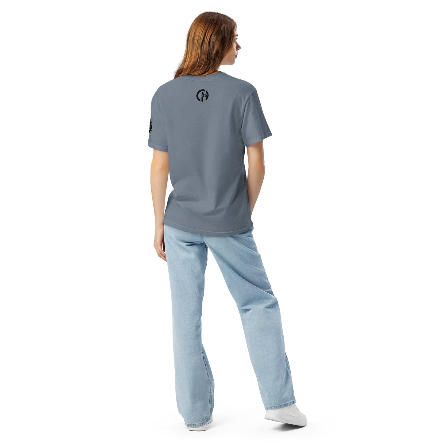 Chillhawk unisex heavyweight short sleeve t-shirt in slate blue - back view of a lady with light skin and long brown hair, is wearing the t-shirt, light blue jeans, and white sneakers. A circular logo is visible on the back side.