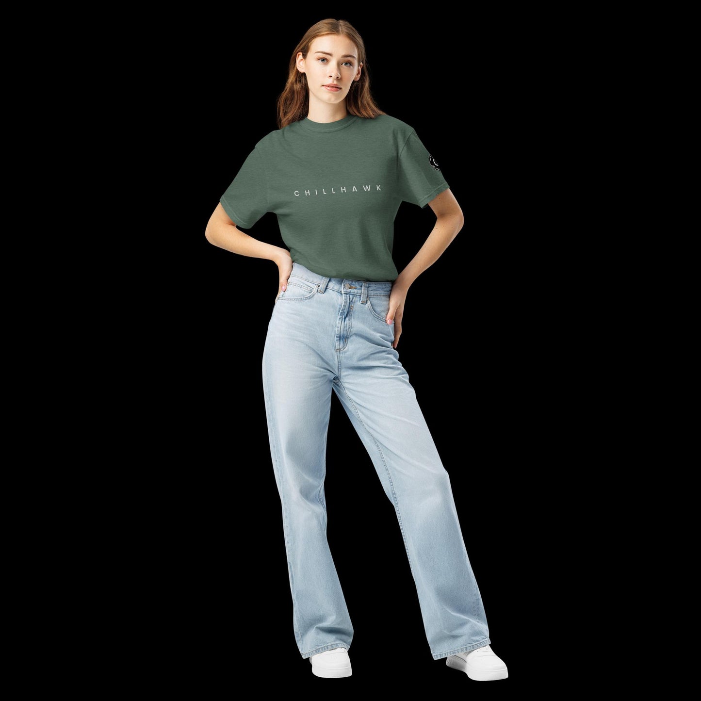 Chillhawk unisex heavyweight short sleeve t-shirt in blue spruce - front view of a lady with light skin and long brown hair, is wearing the t-shirt and light blue jeans. The word "CHILLHAWK" is printed in black on the front of the shirt, and a circular logo is visible on the left sleeve.