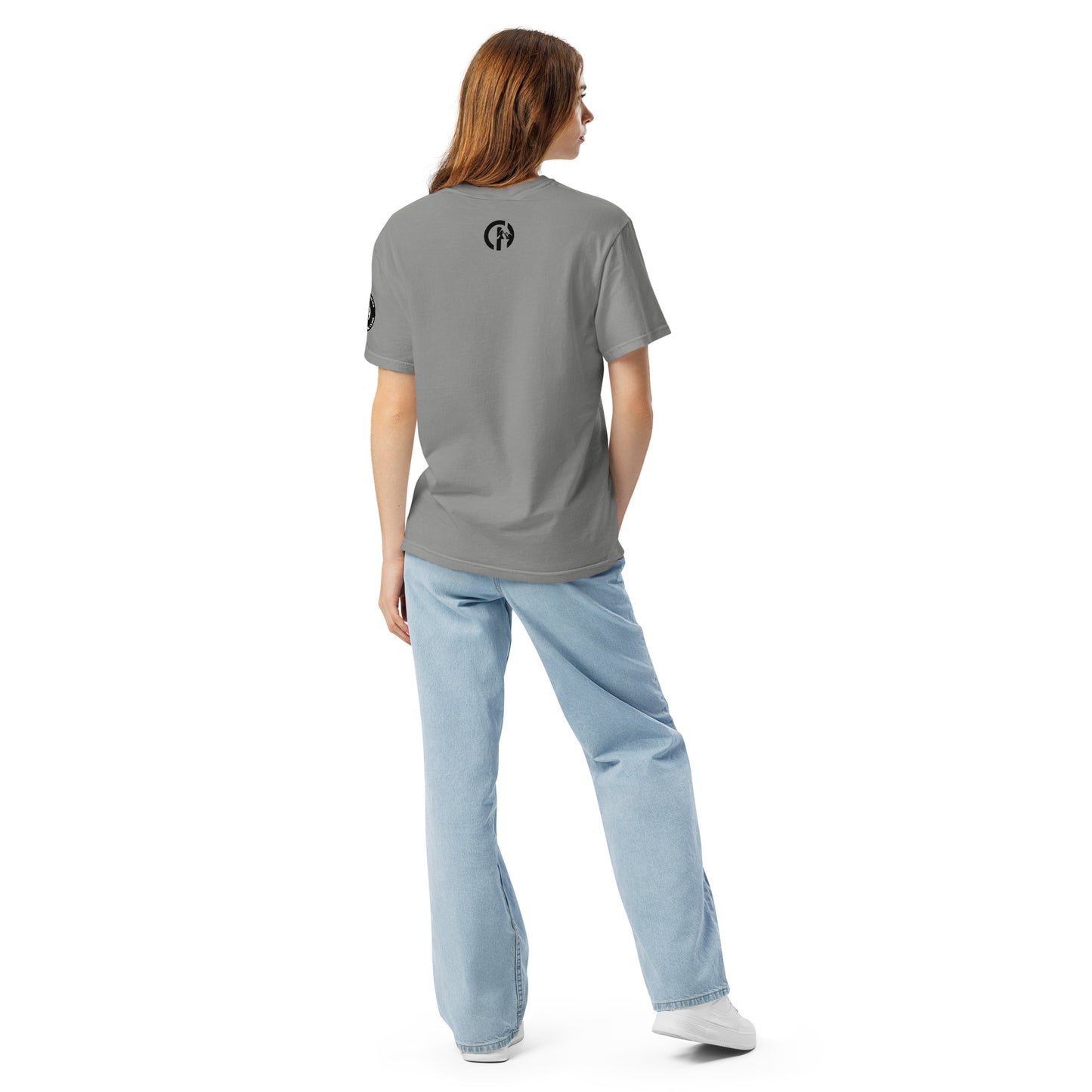 Chillhawk unisex heavyweight short sleeve t-shirt in slate blue - back view of a lady with light skin and long brown hair, is wearing the t-shirt, light blue jeans, and white sneakers. A circular logo is visible on the back side.