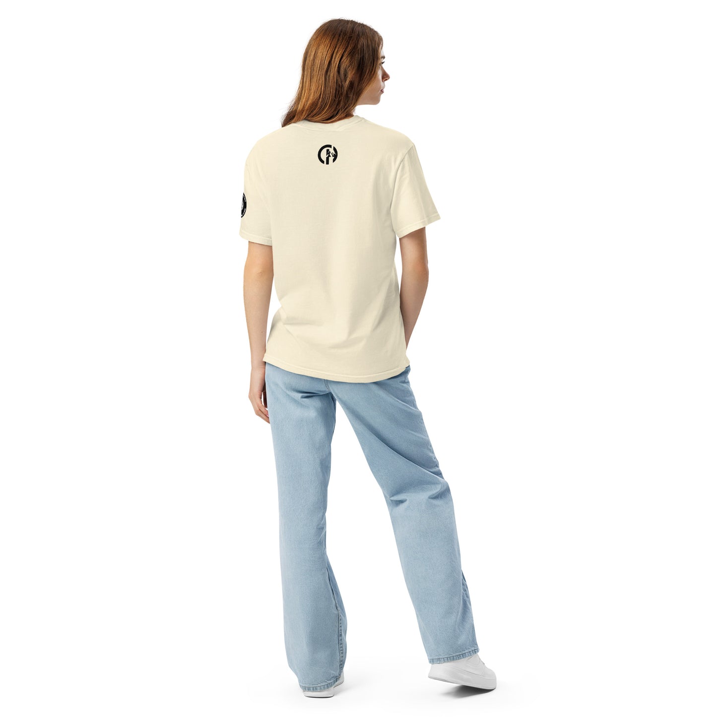 Chillhawk unisex heavyweight short sleeve t-shirt in ivory - back view of a lady with light skin and long brown hair, is wearing the t-shirt, light blue jeans, and white sneakers. A circular logo is visible on the back side.