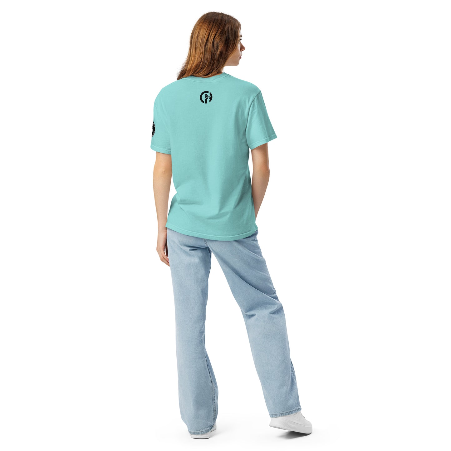 Chillhawk unisex heavyweight short sleeve t-shirt in lagoon blue - back view of a lady with light skin and long brown hair, is wearing the t-shirt, light blue jeans, and white sneakers. A circular logo is visible on the back side.