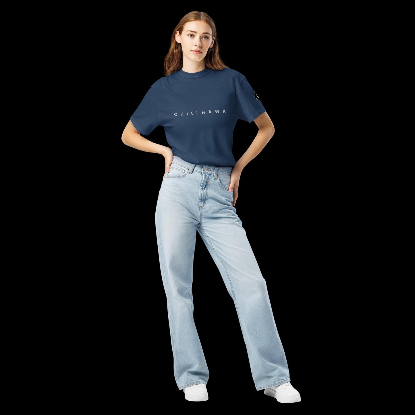 Chillhawk unisex heavyweight short sleeve t-shirt in navy blue - front view of a lady with light skin and long brown hair, is wearing the t-shirt and light blue jeans. The word "CHILLHAWK" is printed in black on the front of the shirt, and a circular logo is visible on the left sleeve.