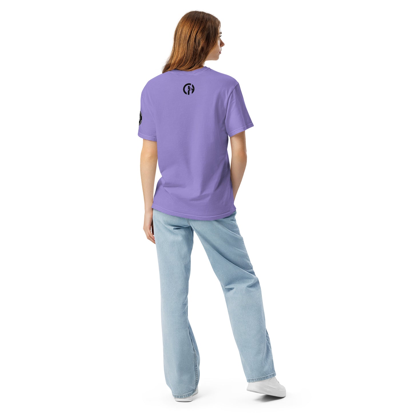 Chillhawk unisex heavyweight short sleeve t-shirt in violet - back view of a lady with light skin and long brown hair, is wearing the t-shirt, light blue jeans, and white sneakers. A circular logo is visible on the back side.