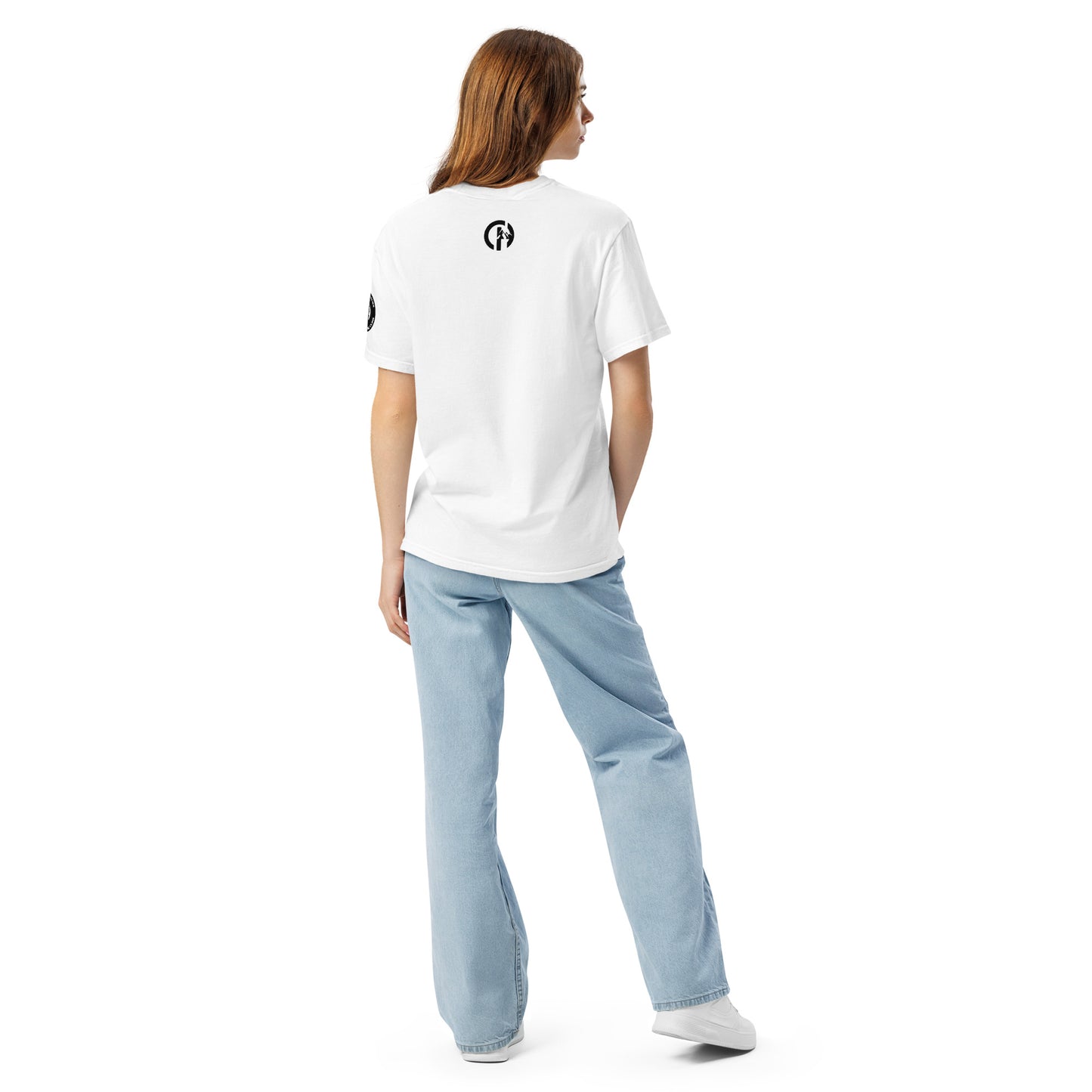 Chillhawk unisex heavyweight short sleeve t-shirt in white - back view of a lady with light skin and long brown hair, is wearing the t-shirt, light blue jeans, and white sneakers. A circular logo is visible on the back side.