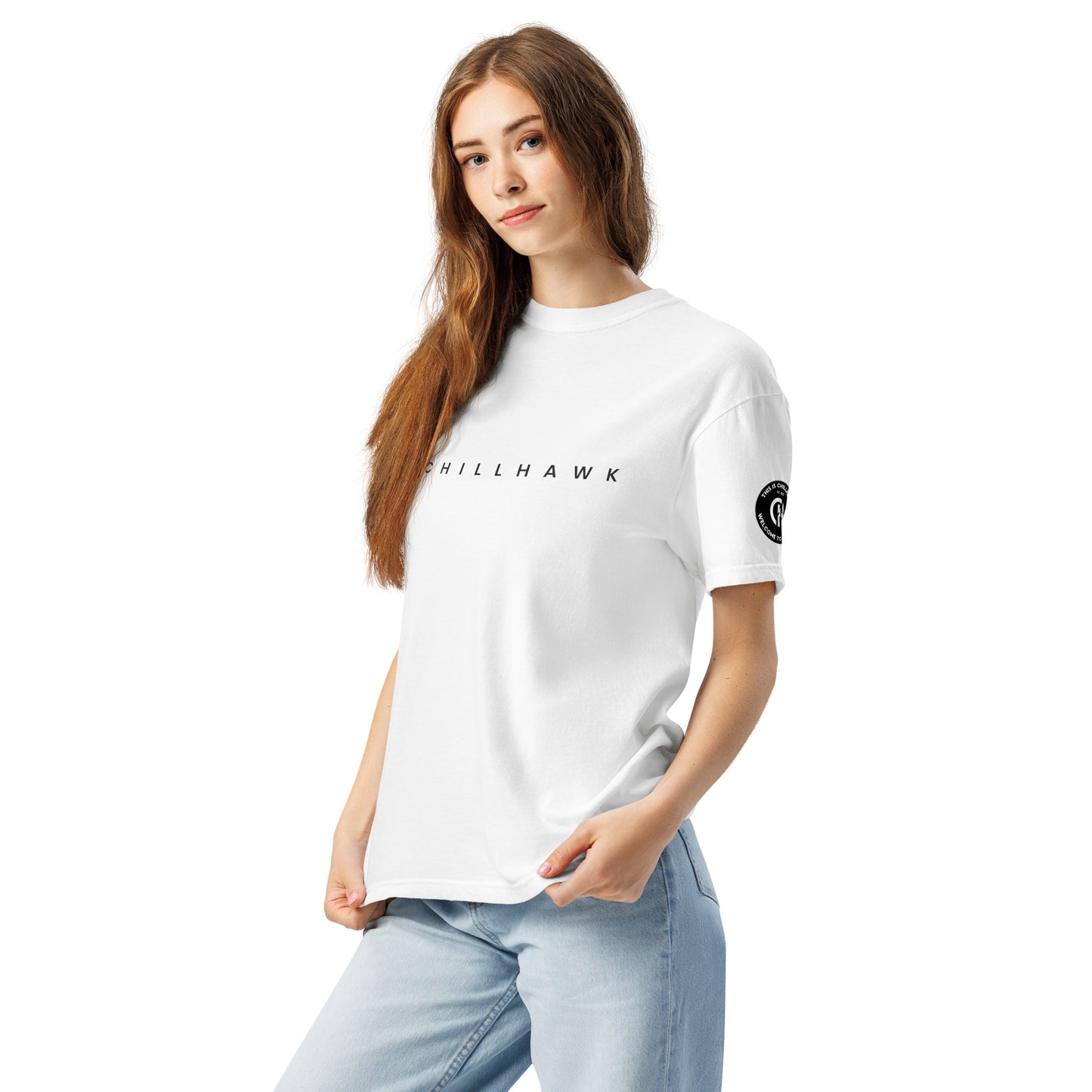 Chillhawk unisex heavyweight short sleeve t-shirt in white - left front view of a lady with light skin and long brown hair, is wearing the t-shirt and light blue jeans. The word "CHILLHAWK" is printed in black on the front of the shirt, and a circular logo is visible on the left sleeve.