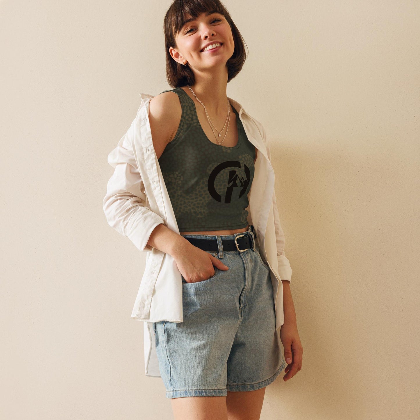 Chillhawk Crop Top White - A lady with light skin and short brown hair, is smiling and wearing a dark green crop top with a circular logo on the chest. The top is designed for performance with a streetwear aesthetic, suitable for workouts, hikes, or post-activity stretches. 