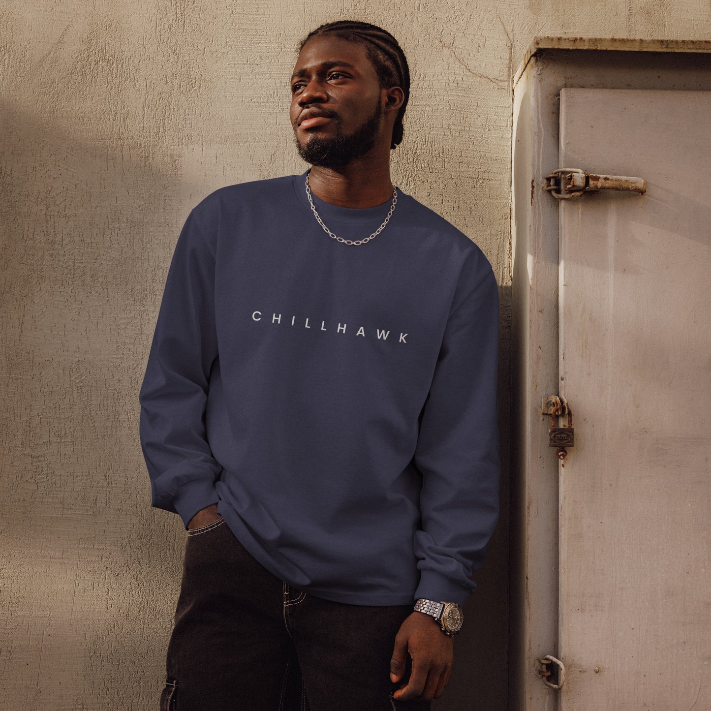 Chillhawk unisex premium heavyweight long sleeve shirt in midnight blue - a person with dark skin and braided hair, is shown looking to the side wearing the shirt and black jeans. The word "CHILLHAWK" is printed in white on the front of the shirt.